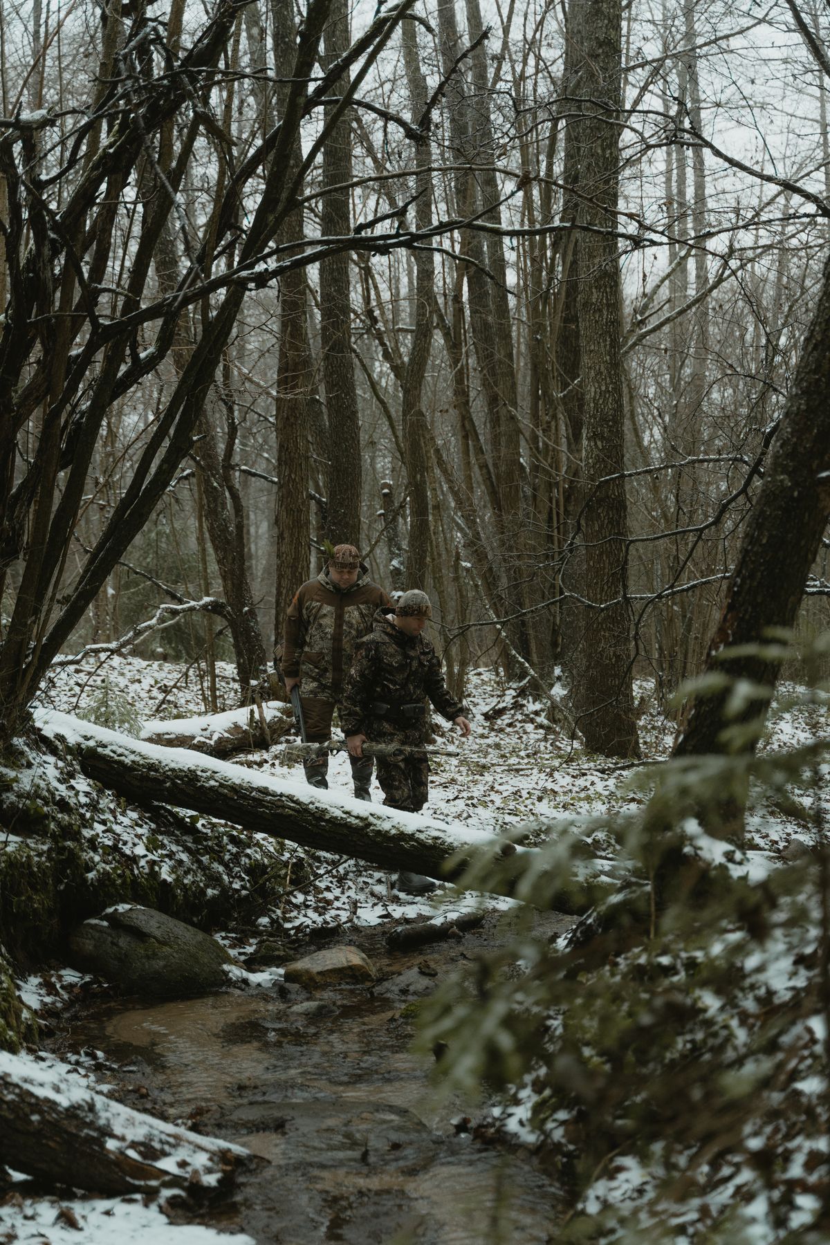 Myśliwi przechodzący przez leśny strumień zimą