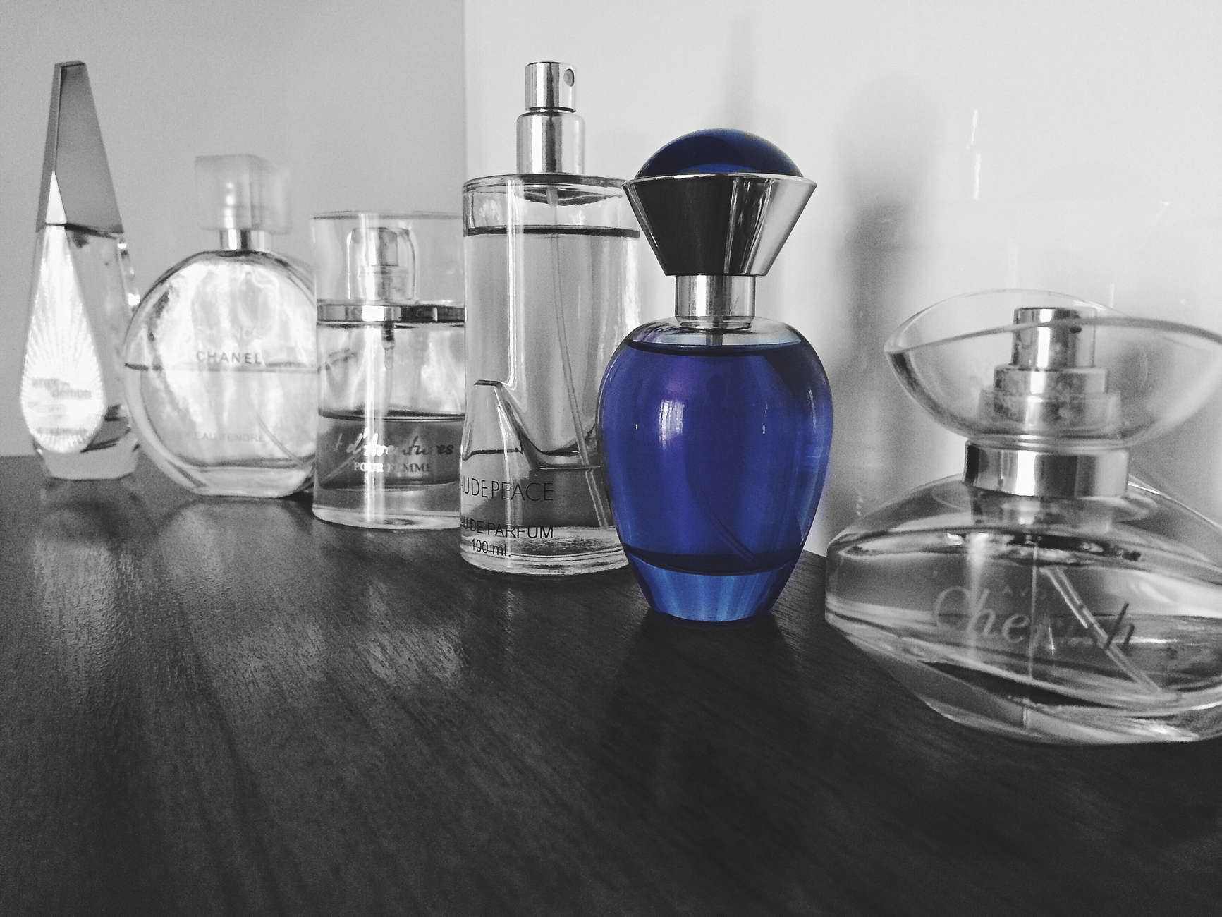 Rzędy eleganckich flakonów perfum w różnych kształtach, w tym butelka o niebieskim kolorze, na ciemnym stole.