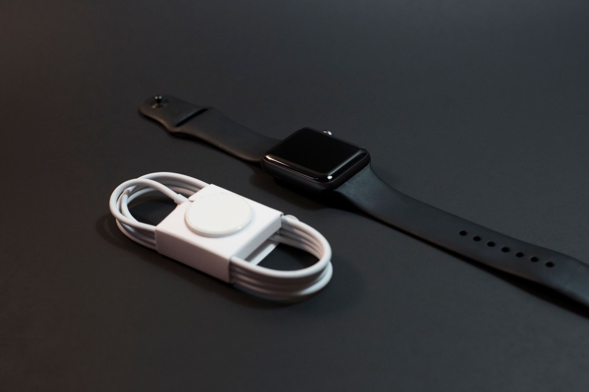 Smartwatch z czarnym paskiem i biała ładowarka na ciemnym tle