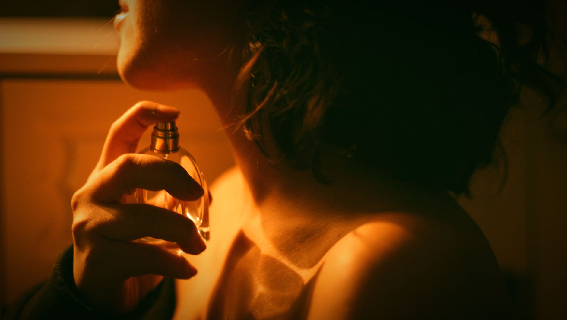 Kobieta w ciemności trzymająca butelkę perfum, oświetlona ciepłym, złotym światłem