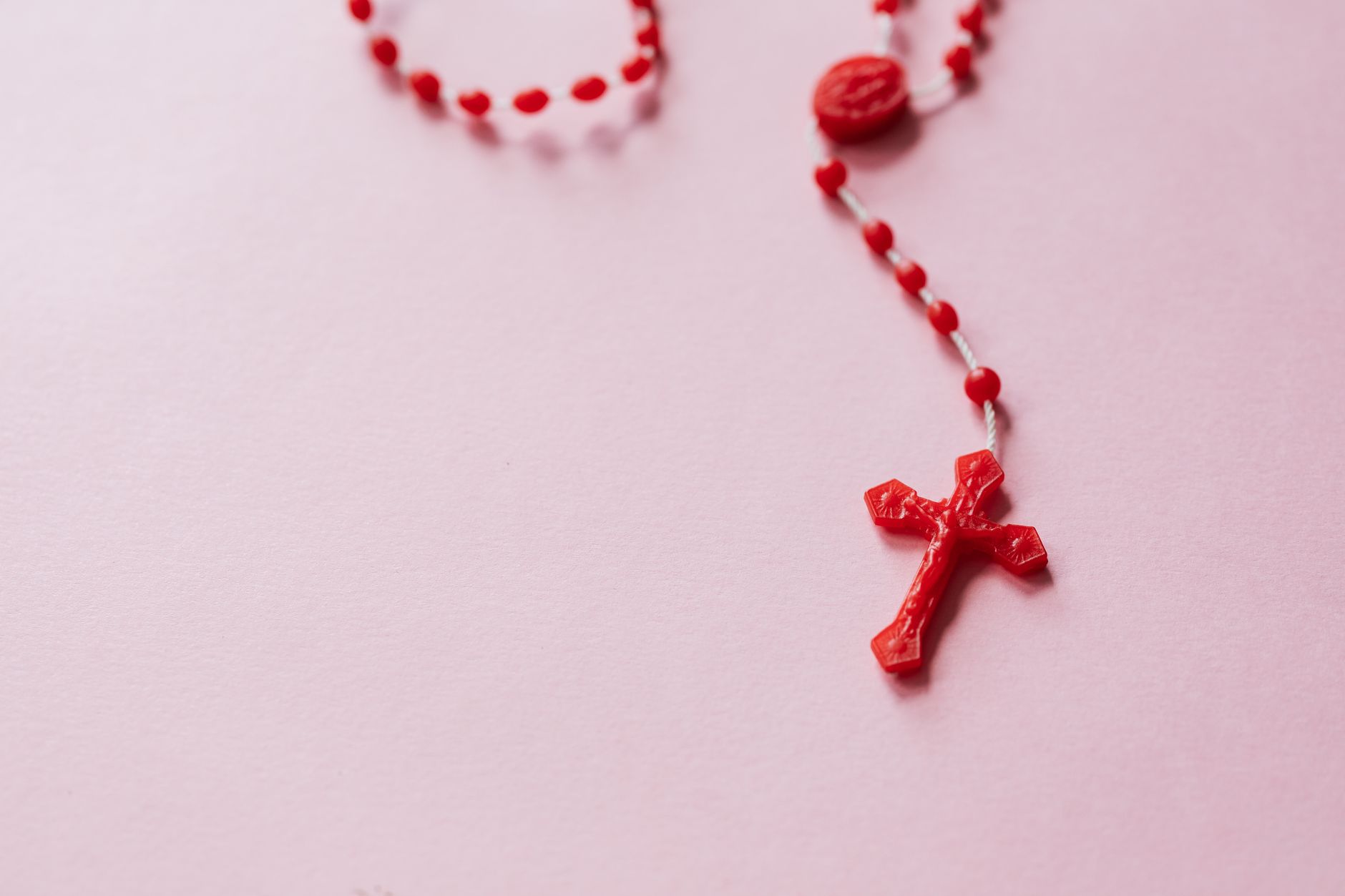 Czerwony różaniec z koralikami na różowym tle, zbliżenie na krzyż