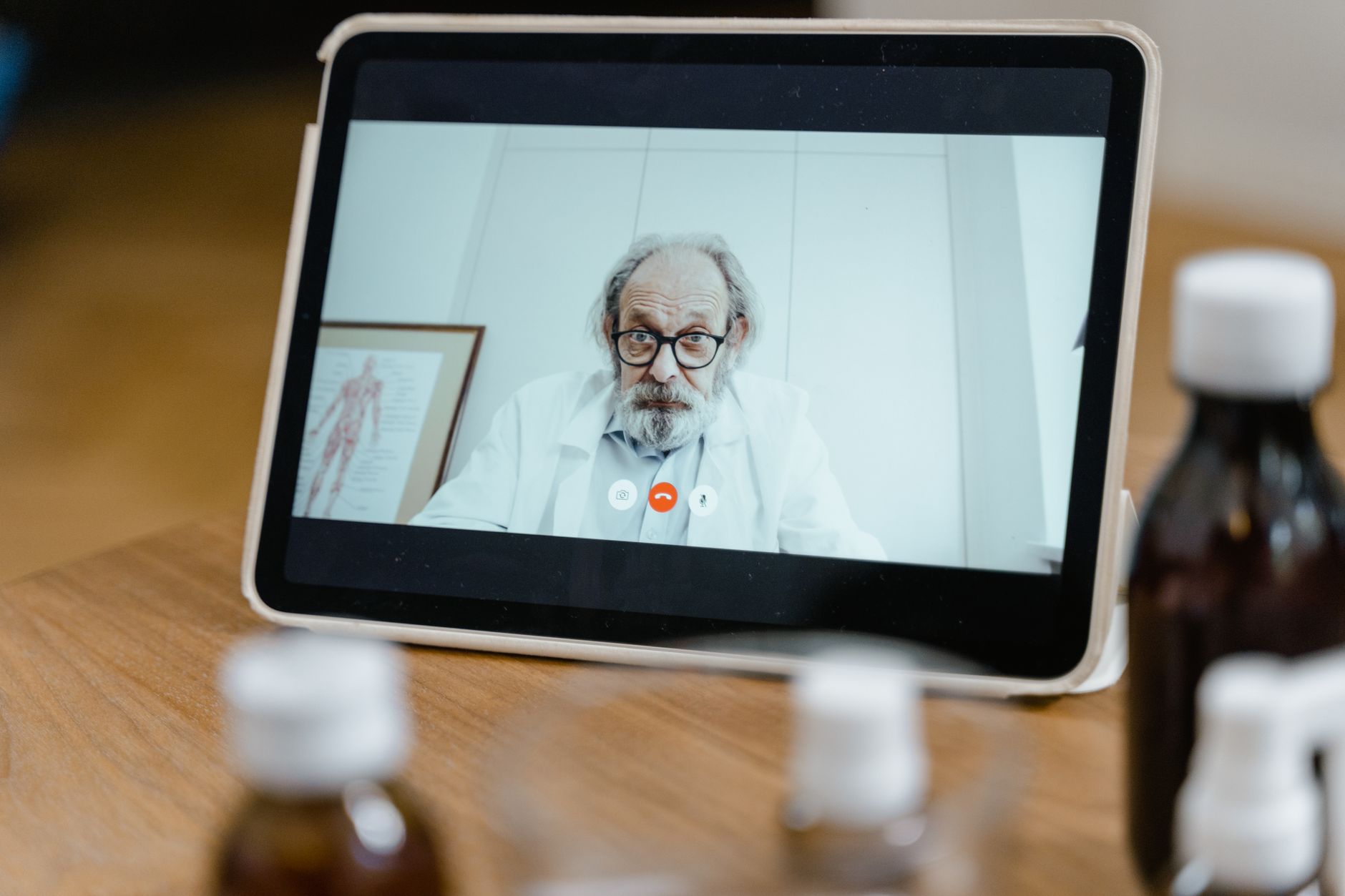 Tablet na drewnianym stole wyświetlający wideokonferencję z starszym lekarzem w okularach i białym kitlu