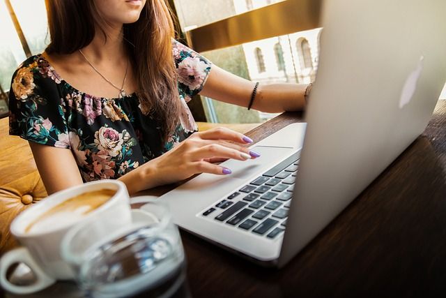 Kobieta pracująca na laptopie przy filiżance kawy w kawiarni