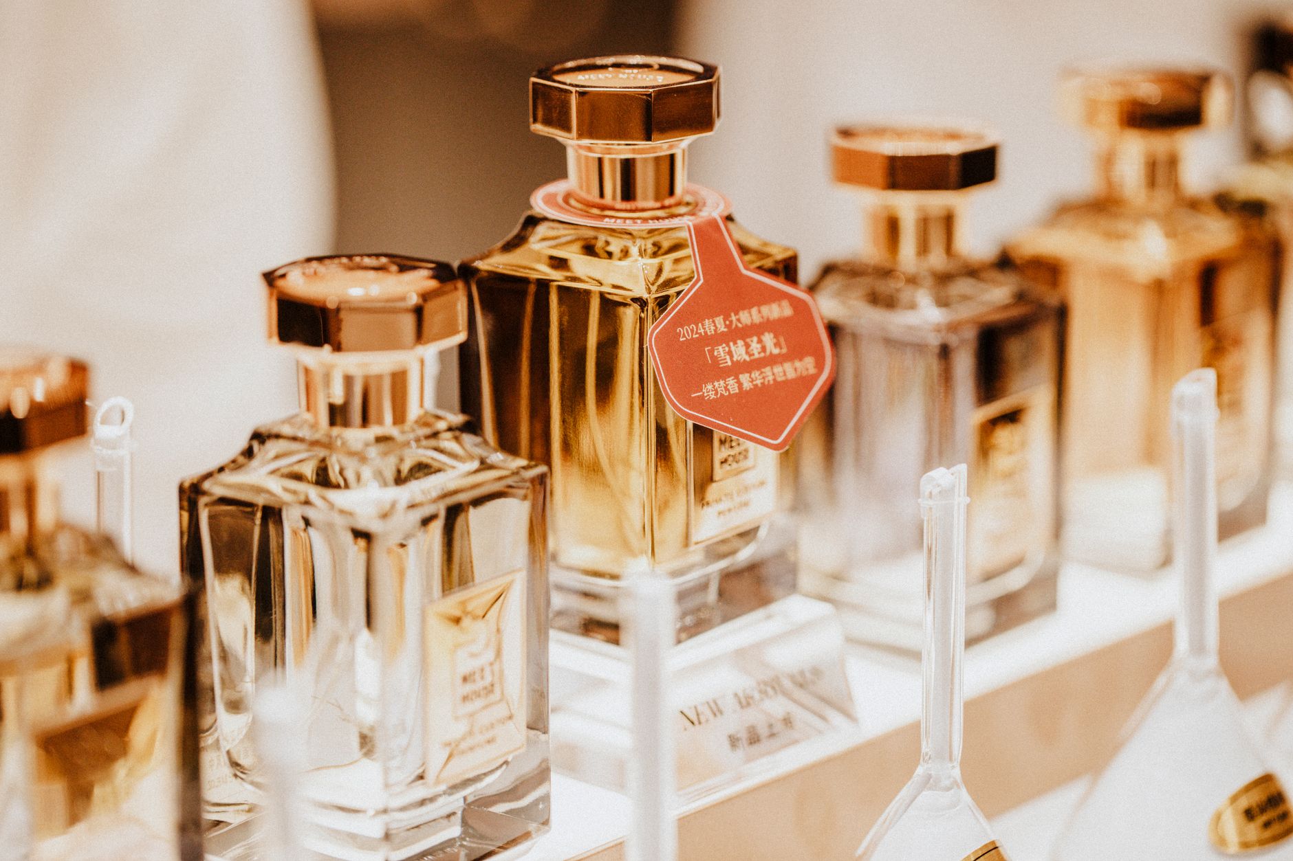 Kolekcja butelek perfum o złotych zamknięciach ustawionych na białej półce, jedna z czerwoną etykietą