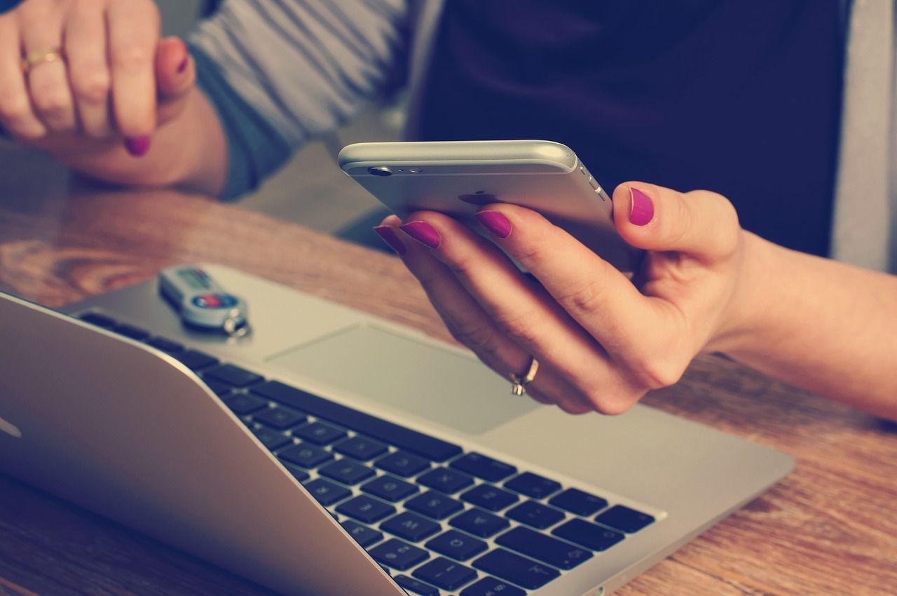 Kobieta trzymająca smartfon obok laptopa przy drewnianym biurku