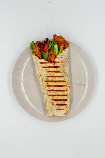 Tortilla zawita z pieczonym mięsem i warzywami na białym talerzu, podawana z sosem grillowym